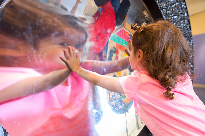 A visitor observes their reflection in a warped mirror in the Young Explorers Area