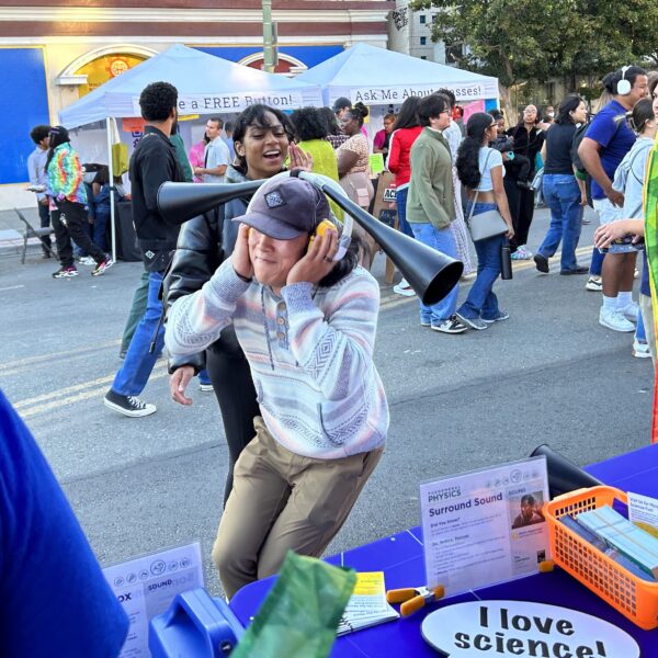 A person participates in a science festival by listening through a large, black acoustic listening device.