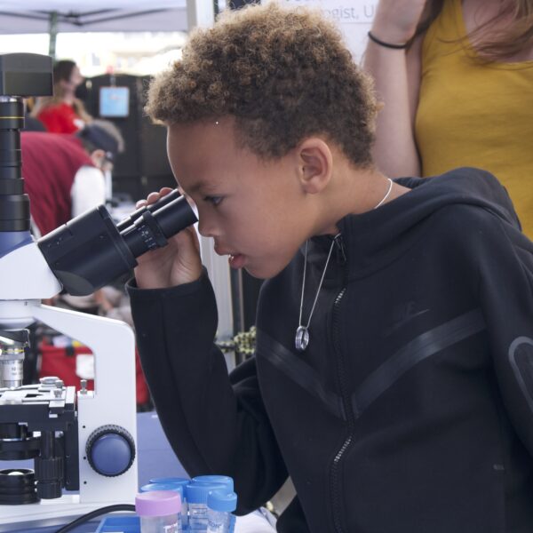 A child is looking through a microscope at an outdoor science event.