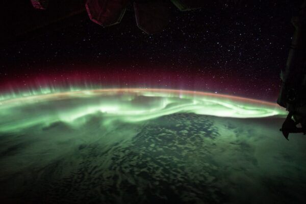 A vibrant green and red aurora spans the curvature of the Earth, as seen from the International Space Station