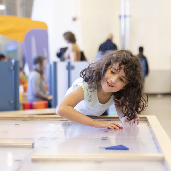 A young visitor plays with shapes on an air table in the Playtopia Juegolandia exhibit