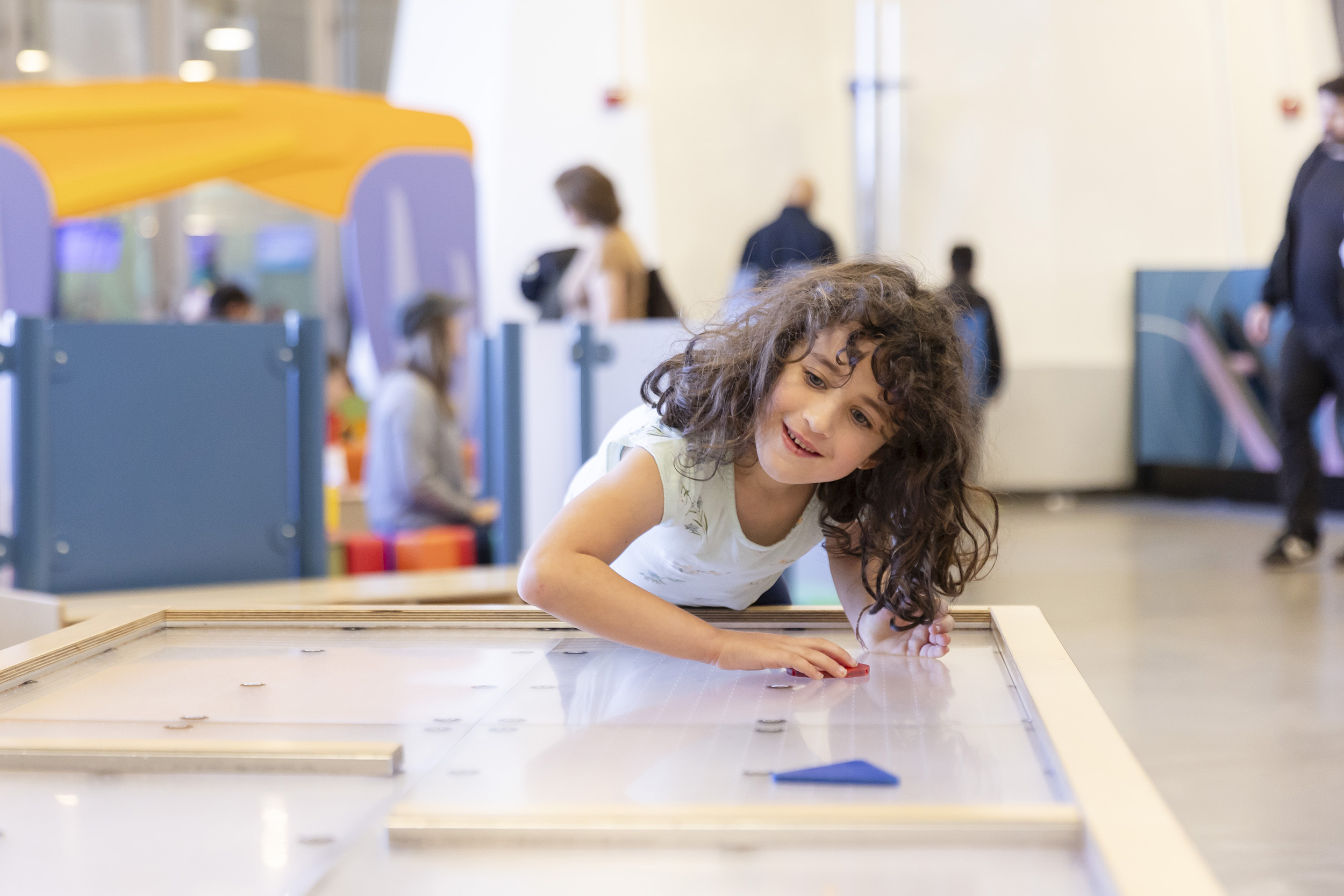 A young visitor plays with shapes on an air table in the Playtopia Juegolandia exhibit
