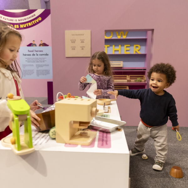 hree children engaging in play at an interactive exhibit featuring a pretend kitchen setup.