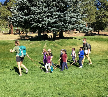 Children and adults walking in a line through a green space.