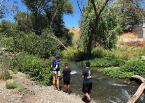 Two youth look out over a river with an adult. 