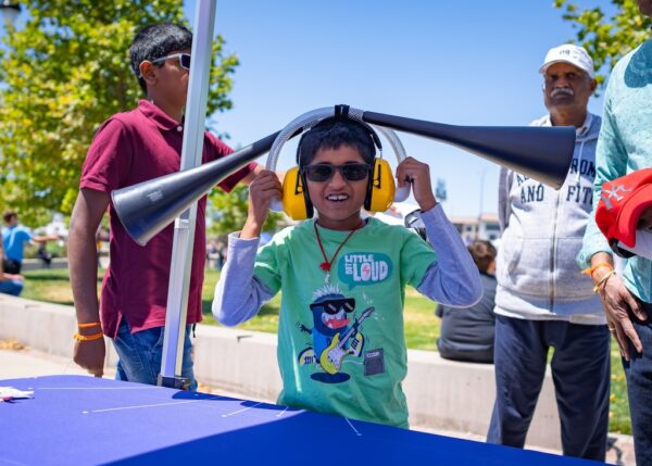 Child at an outdoor event wearing yellow headphones with two funnels attached.
