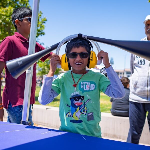 Child at an outdoor event wearing yellow headphones with two funnels attached.