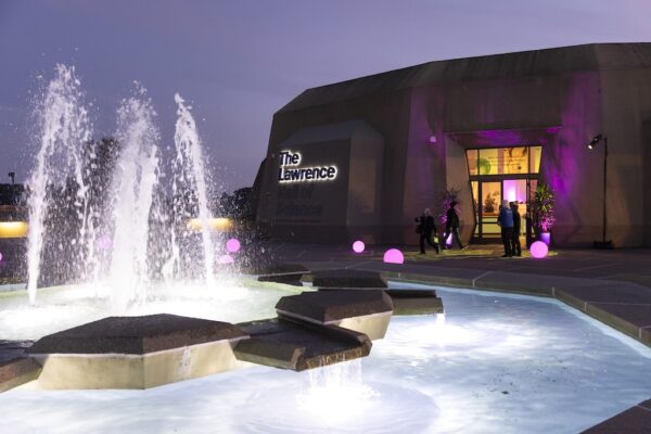 Fountain and purple-lit entrance of The Lawrence Hall of Science at night.