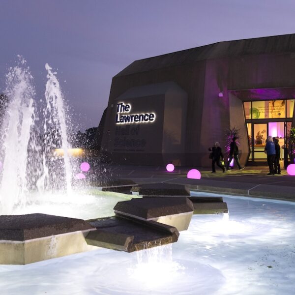 Fountain and purple-lit entrance of The Lawrence Hall of Science at night.