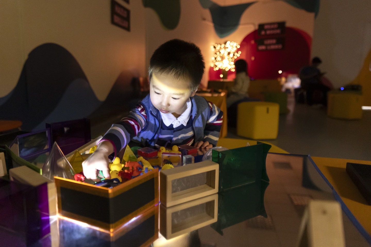 Young boy sorting through colorful translucent toys and building blocks at an illuminated play station during the Glowtastic exhibit