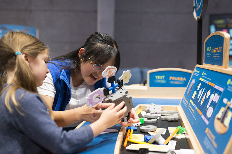 A Lawrence volunteer collaborates with a visitor to build a contraption