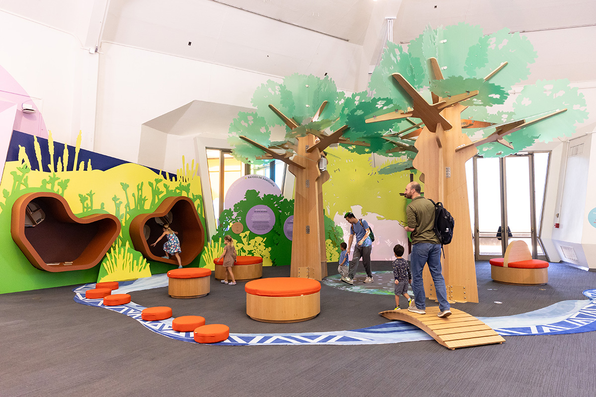 Visitors explore the yuutka exhibit, featuring three large tree-like structures, two reading nooks, and other elements.