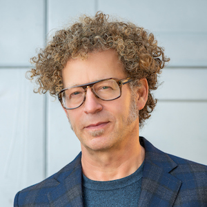 Portrait of Ken Goldberg, with curly hair and dark-framed glasses, wearing a blue blazer.